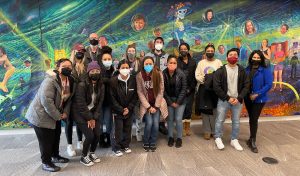 A photo of a class of students posing in front of a colorful mural.